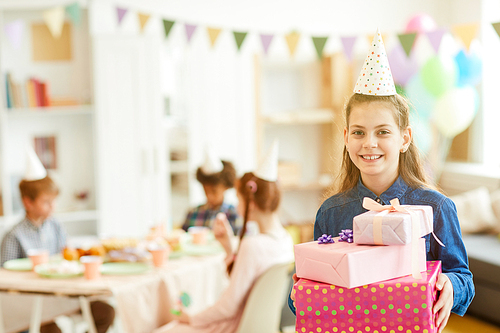 Waist up  portrait of happy teenage girl holding gift boxes posing during birthday party with friends, copy space