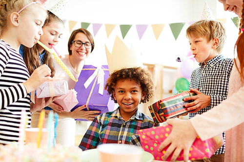 Portrait of happy African-American boy receiving gifts surrounded by friends at Birthday party, copy space