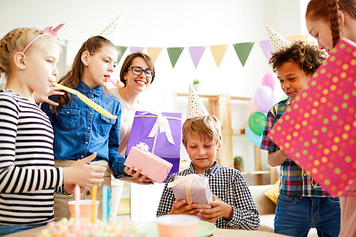Portrait of happy boy receiving gifts surrounded by friends during Birthday party, copy space