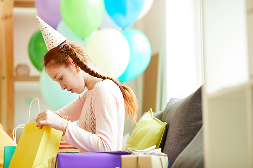 Side view portrait of red haired girl opening gifts at Birthday  party, copy space