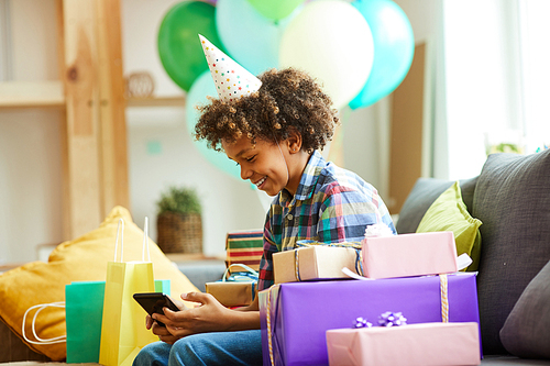 Side view portrait of smiling African-American boy opening presents at Birthday  party, copy space