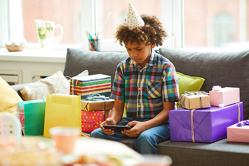 Portrait of African-American boy using smartphone while  opening presents  at Birthday  party, copy space