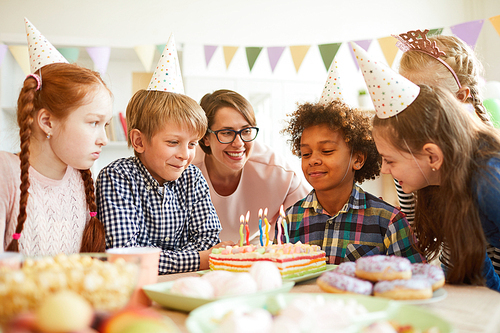Portrait of happy African-American boy blowing candles on Birthday cake during party  with friends , copy space