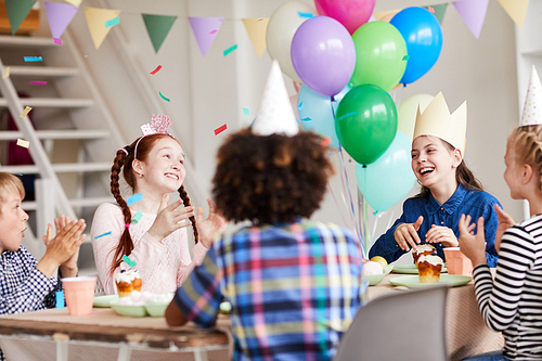 Group of happy children having fun during Birthday party in decorated room with confetti, copy space