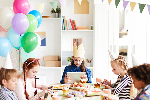 Multi ethnic group of children using internet sitting at table during Birthday party, gadget obsession concept, copy space