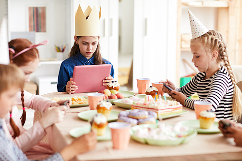 Group of children using internet sitting at table during Birthday party, gadget obsession concept, copy space