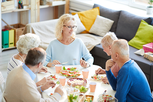 Happy attractive mature woman with blond curly hair sitting at table and enjoying dinner with friends