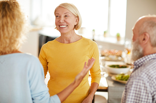 Positive excited attractive mature lady with short blond hair listening to friends while welcoming them to home