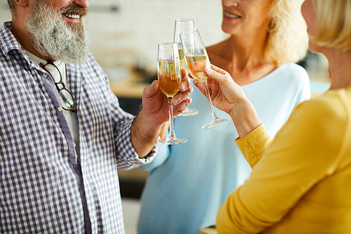 Close-up of positive mature friends standing in circle and clinking champagne flutes together