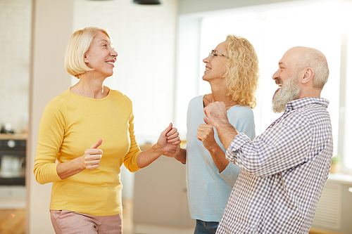 Positive active seniors in casual outfits dancing boogie-woogie in modern flat while having fun together on weekend