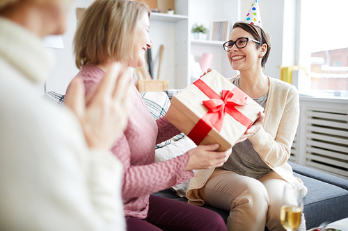 Portrait of three cheerful women celebrating birthday at home focus on young woman holding gift box, copy space