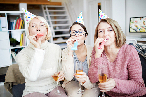 Portrait of three happy women blowing party horns and  while celebrating birthday at home