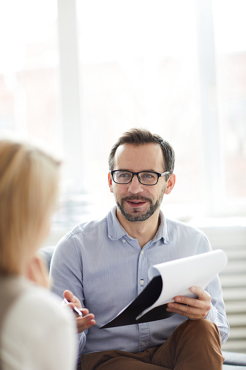 Confident counselor with document giving advice to his patient while discussing ways of solving her problem