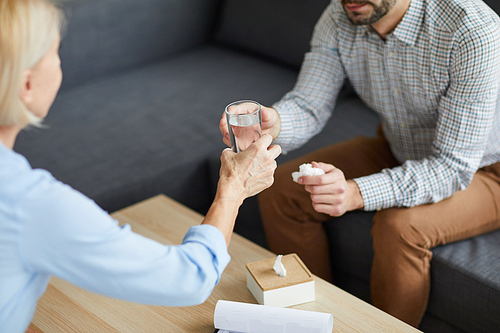 Mature counselor passing glass of water to patient over table during discussion of his problems