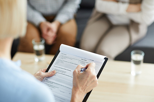 Mature counselor with pen putting ticks in document while filling it in during family consultation