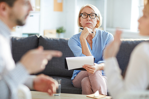 Serious mature blonde female listening attentively to young couple argument while sitting in front of them