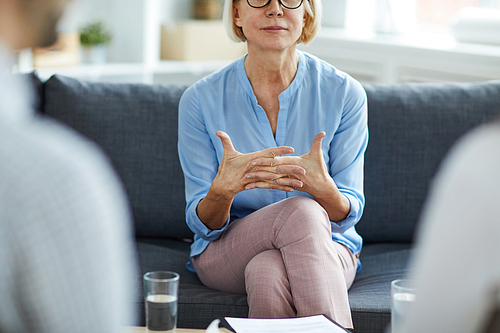 Mature professional psychologist sitting on couch in front of her patients and giving them advice