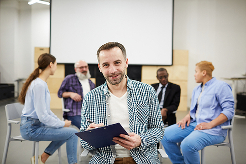 Portrait of mature male psychologist smiling at camera while leading therapy group, copy space