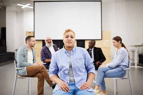 Portrait of masculine woman  while sitting in chair in front of therapy group, copy space