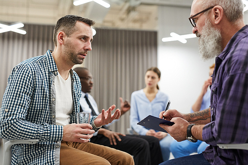 Side view portrait of two mature men sharing problems with psychologist during group therapy session, copy space