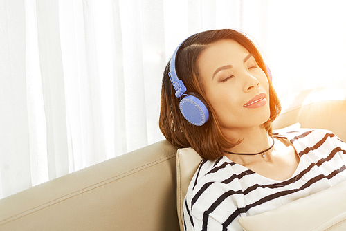 Pretty young Vietnamese woman smiling when enjoying music in headphones