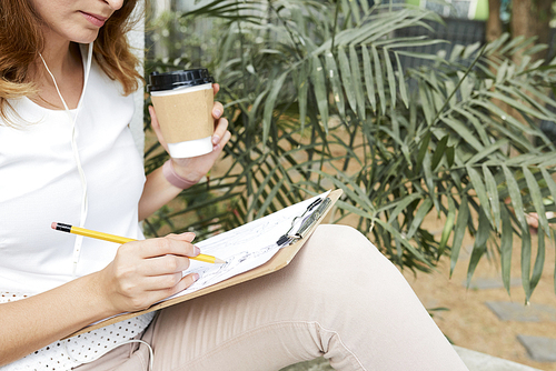 Female freelancer drawing sketch and drinking take-away coffee in park