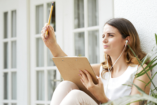 Creative young woman closing one eye and using pencil to measure an object that is far from her