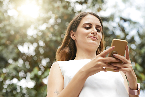 Pretty young woman reading text messages on her phone when standing outdoors