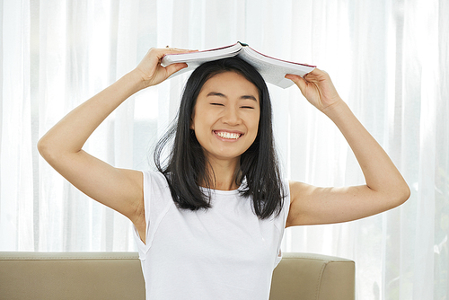 Cheerful Asian college student opening book over her head