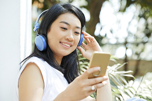 Smiling pretty young woman in headphone choosing song to listen in smartphone application