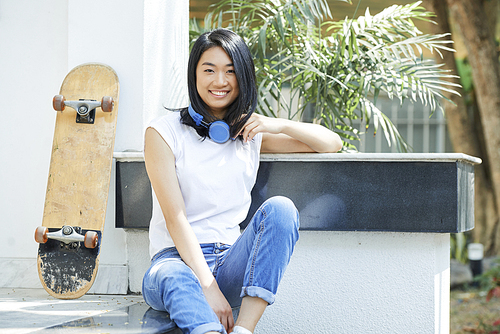 Smiling lovely college student resting on steps after riding on skateboard