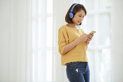 Pretty Vietnamese teenage girl using mobile app to choose music to listen in her new headphones