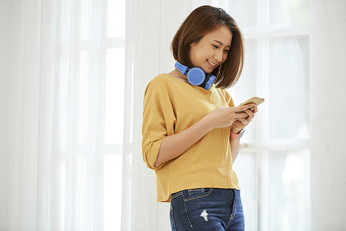 Lovely young Asian woman smiling and reading text message from boyfriend