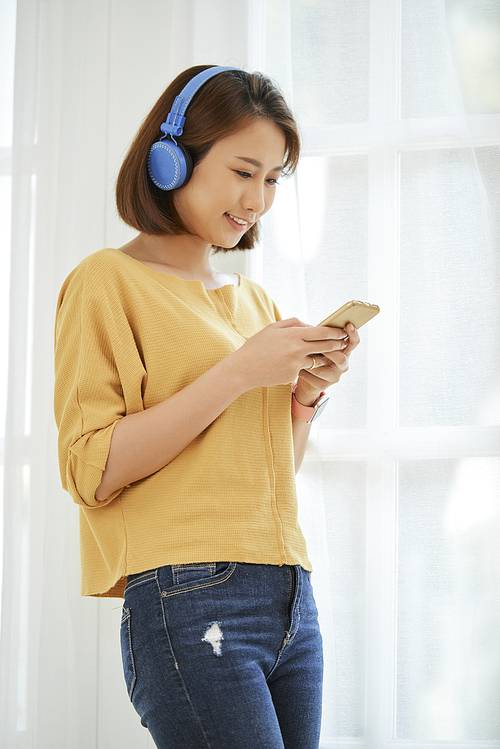 Vietnamese teenage girl in headphones smiling when texting friends