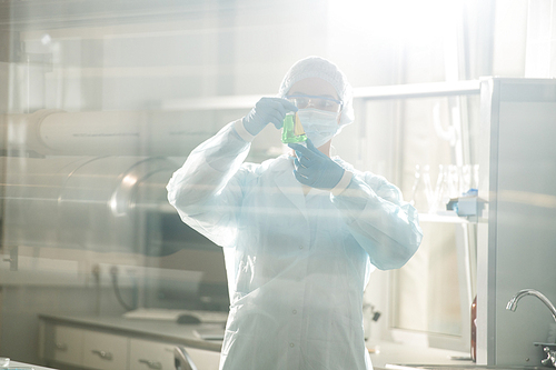 Serious busy young female chemist in protective goggles and mask doing laboratory testing for researching infection in closed laboratory