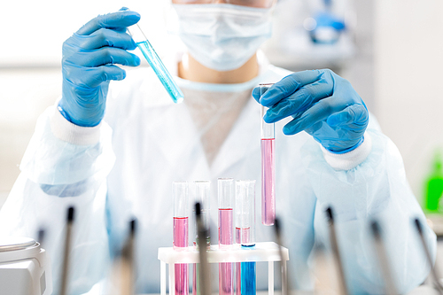 Close-up of unrecognizable woman in sterile gloves working with hazardous liquids in test tubes while testing new medications in laboratory