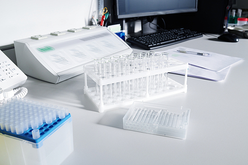 Laboratory glassware, test tube rack, container, electrical device, computer and papers on table of scientist