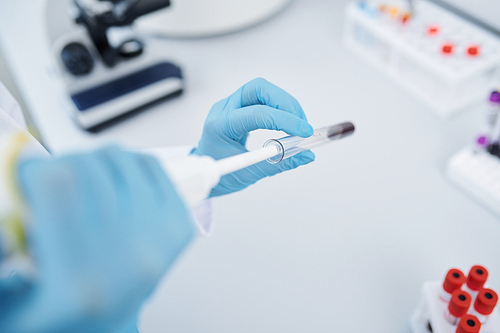 Close-up of unrecognizable laboratory researcher in sterile gloves dropping blood into test tube and performing blood test in laboratory