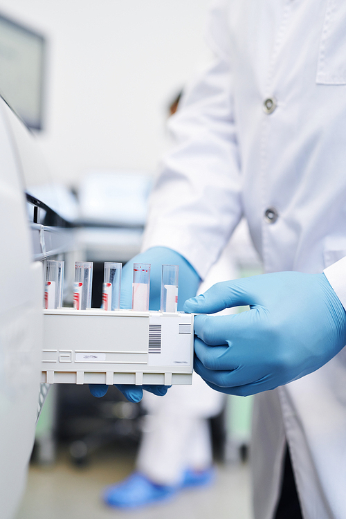 Close-up of unrecognizable lab technician in white coat and rubber gloves putting test tube section into modern medical machine for scanning samples