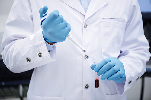 Close-up of unrecognizable medical doctor in white coat and surgical gloves dropping blood into test tube, saving life in donation center concept