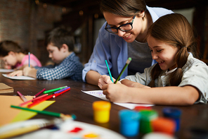 Portrait of smiling young woman working with kids drawing in art class, copy space