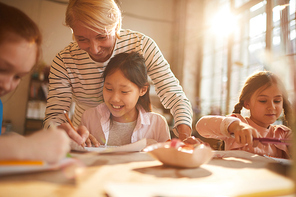 Portrait of woman working with group of little girls painting in art class, scene lit by serene sunlight, copy space