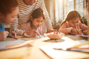 Portrait of cute Asian girl drawing picture in art class for children, scene lit by serene sunlight