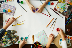 Top view of childrens hands over background with art supplies, paints and brushes over white paper, copy space