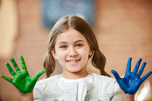 Portrait of cute little girl showing hands colored with paint and , finger painting and creativity concept