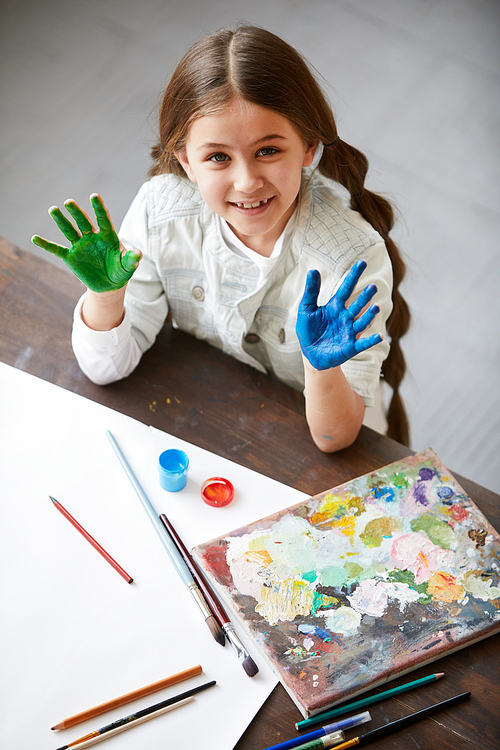 High angle portrait of cute little girl showing hands colored with paint and , finger painting and creativity concept