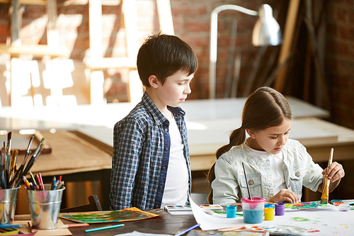 Portrait of two children boy and girl painting together standing at table at home, copy space