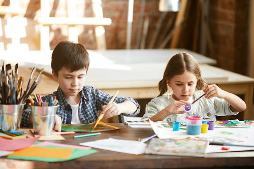 Portrait of two children boy and girl painting together sitting at table at home, copy space