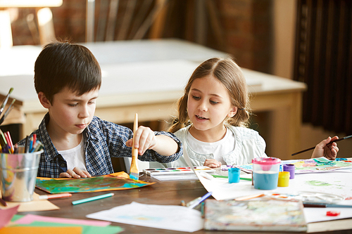 Portrait of two children boy and girl painting together sitting at table at home