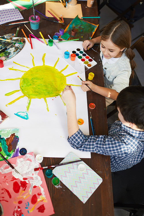 High angle portrait of two children drawing sun while painting picture together, copy space